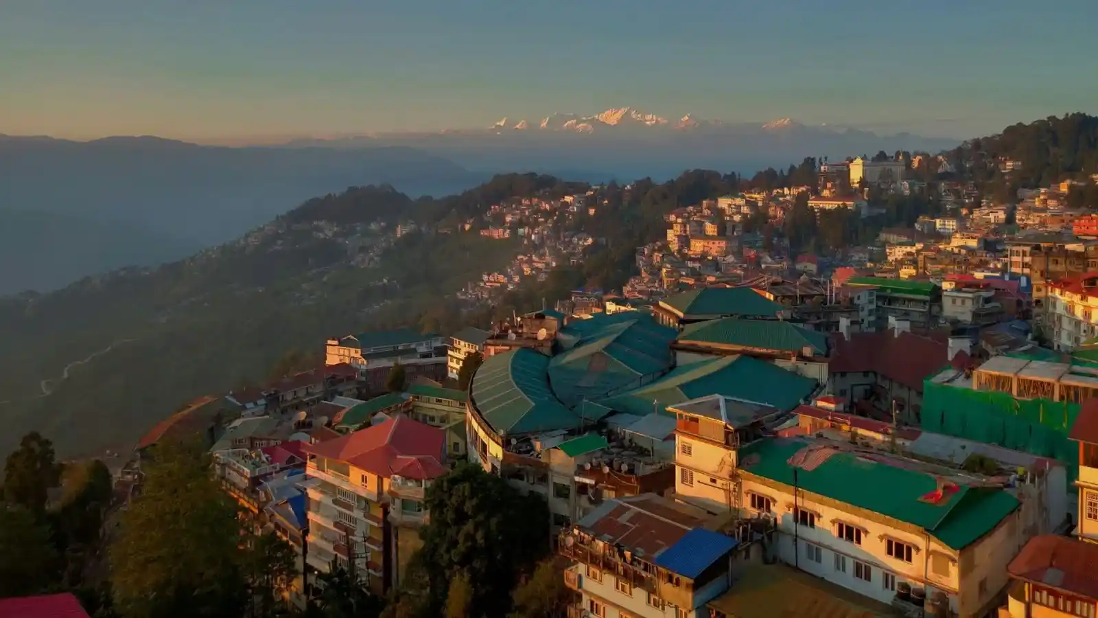 Aerial view of Darjeeling town's colourful rooftops on a ridge with the Kangchenjunga range at sunrise