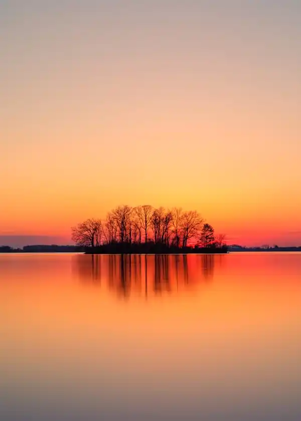 Orange sunset reflecting over a calm lake with a small tree-covered island