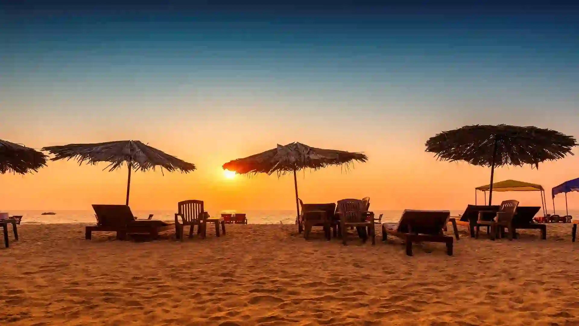 Beach chairs with thatched umbrellas at Goa beach sunset