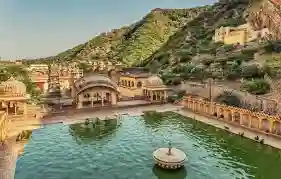 Ancient stepwell with arched pavilions and green water below forested hills near Amber, Jaipur