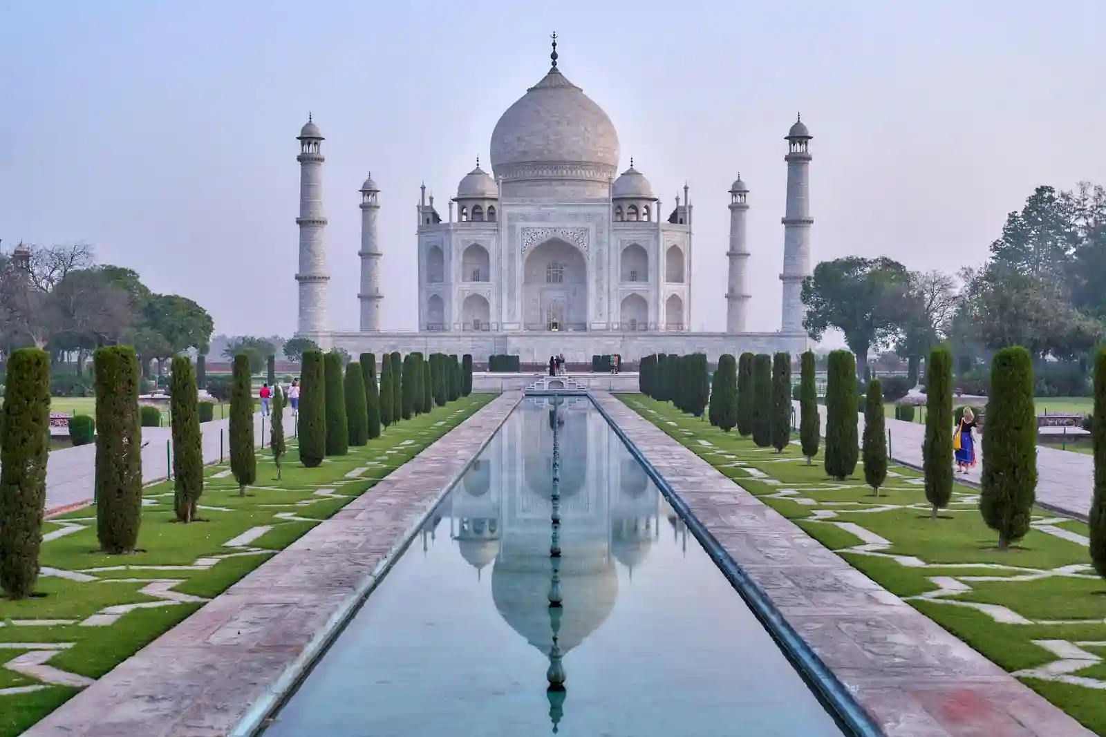 The white marble Taj Mahal in Agra mirrored in the central reflecting pool with garden cypress trees on either side